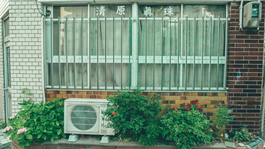 Street view of a building facade with an air conditioning unit and greenery.